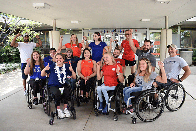 group of fourteen Paralympic athletes, some in wheelchairs and some standing, posing and looking excited