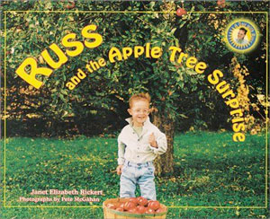 young boy standing in front of apple tree with bushel basket full of apples
