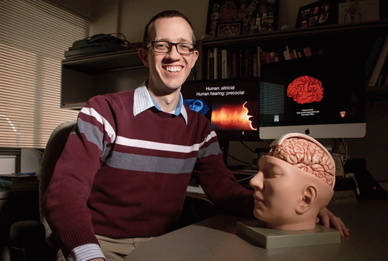 Dr. Brian Monson seated next to model of head with exposed brain