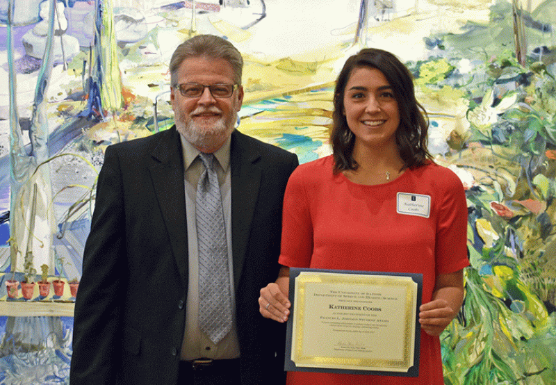 Dr. Ron Chambers standing next to young woman who is holding a scholarship, in front of an abstract painting