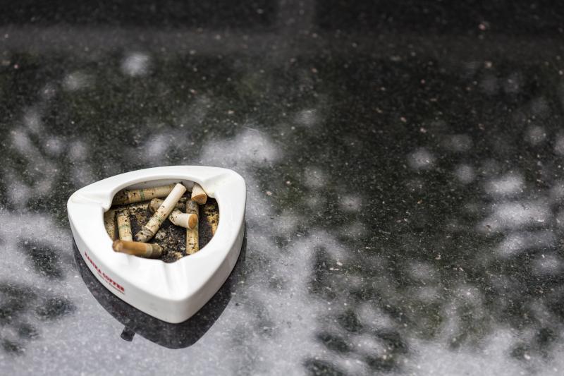 An ashtray with cigarettes sits on a gray floor. 