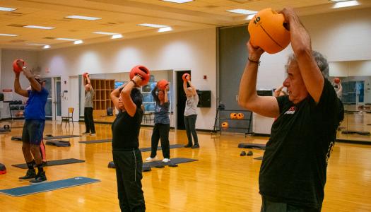 Members of the Lifetime Fitness Program swing medicine balls overhead for an upper body exercise. Classes in the spring and fall terms are hosted at the Campus Recreation Center East in Urbana.
